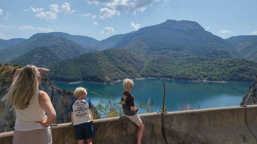 A woman and two children look out over a turquoise mountain lake from a viewpoint.