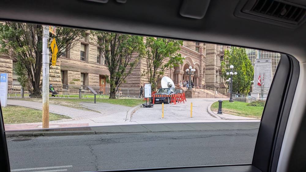 A picture of a flying saucer coming out of the roof of a car parked outside a building.