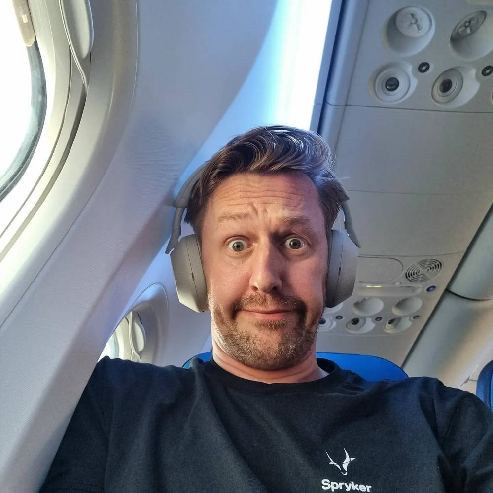 Guido making a surprised face in a selfie while wearing headphones on an airplane.