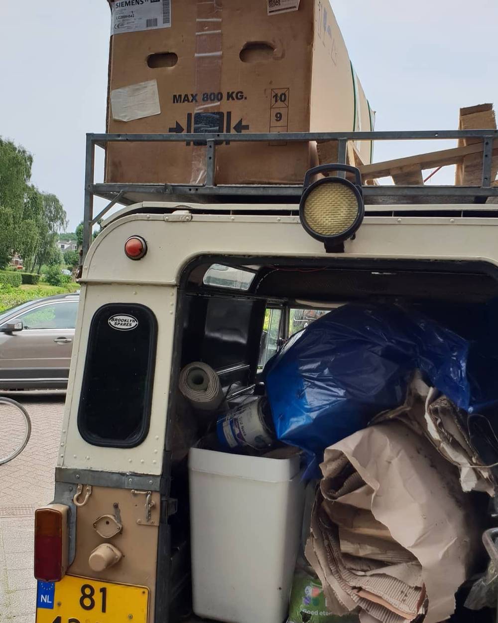 The back of a Land Rover loaded with bags and a bin, parked on a street.
