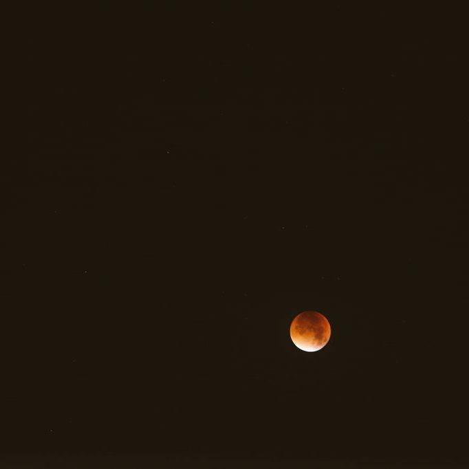 A reddish blood moon during a lunar eclipse, seen against a dark night sky.