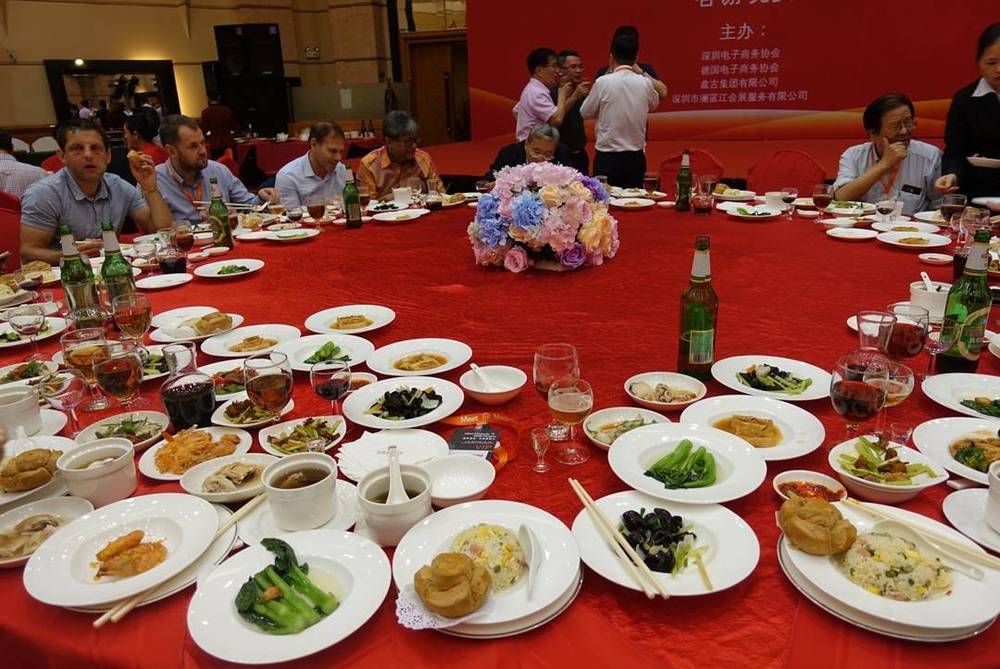 A round banquet table filled with Chinese dishes, drinks and a floral centerpiece.