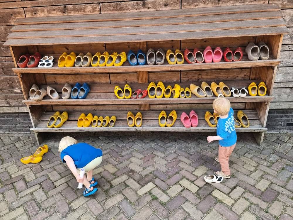 Two children looking at a wooden shelf filled with rows of colorful traditional Dutch clogs.