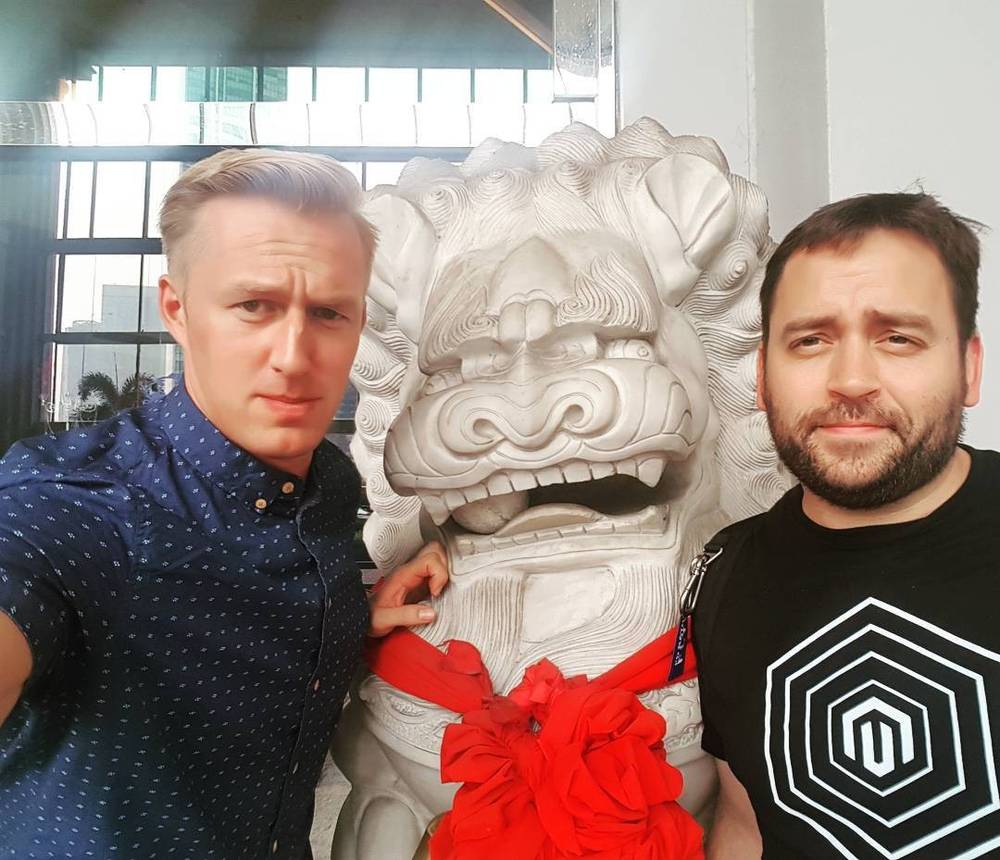 Two men posing beside a large stone lion statue.
