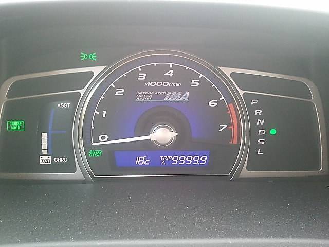 A car's dashboard shows a hybrid drive gauge and an odometer reading near 10,000 km.