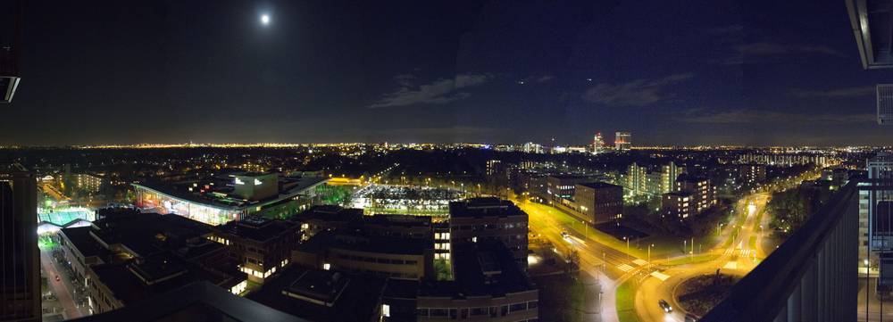 A wide night panorama shows Hoofddorp's streets and rooftops from a high vantage point.