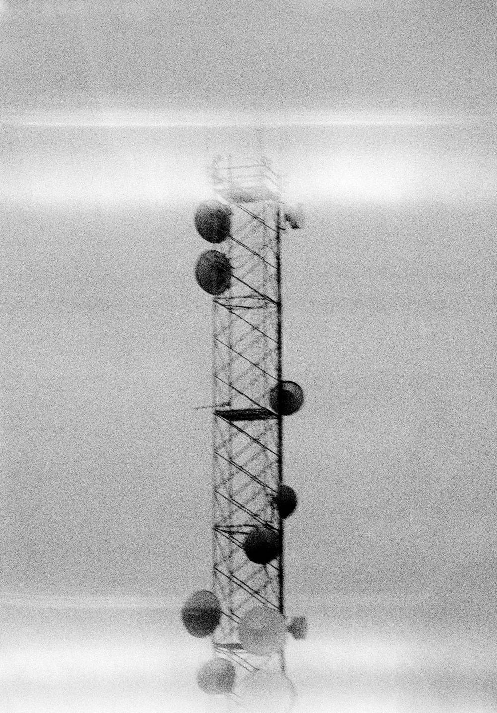 TV transmission tower shot from a distance in grainy B&W. it's out of focus and light leaks run horizontally across the frame, suggesting a transmission