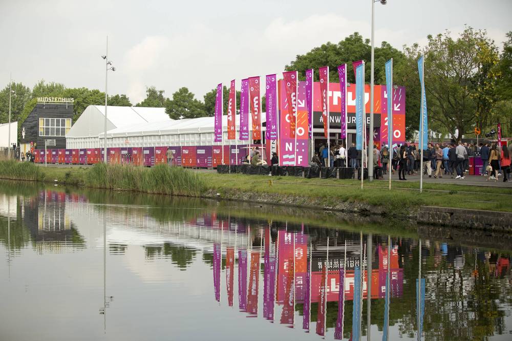 TNW Europe conference tents and flags reflect in a canal beside a historic brick building.