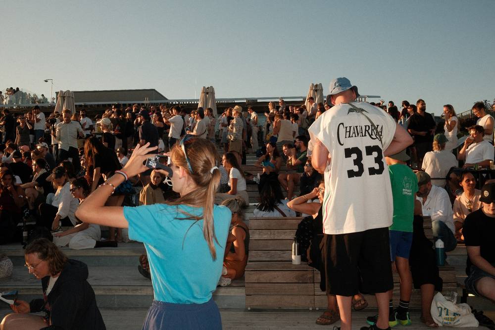 Two people standing in front of a crowd taking sun photos with eclipse glasses