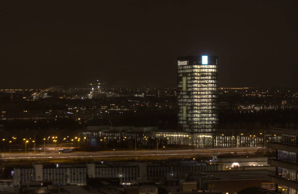 A tall illuminated office tower stands out against the night sky above a highway.