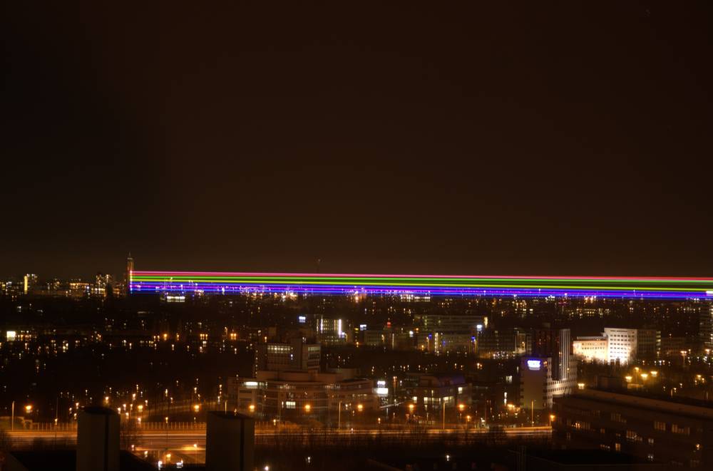 Colored laser beams sweep low across the night skyline of Utrecht.