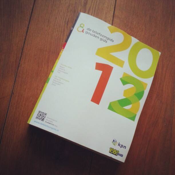 A Dutch phone directory booklet ('de Telefoongids en Gouden Gids 2013') lying on a wooden table.