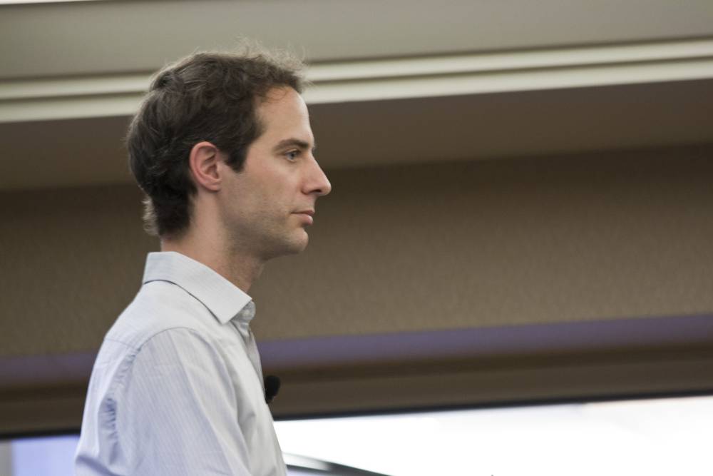 A man in profile with short hair sits attentively in a conference room.