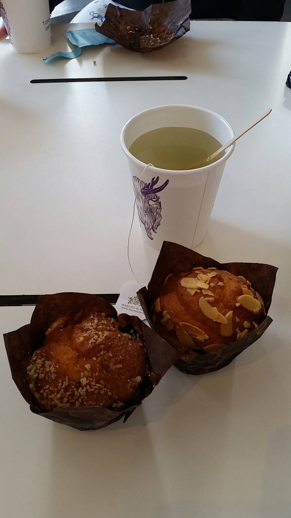 Two muffins and a drink sit on a table beside conference materials.