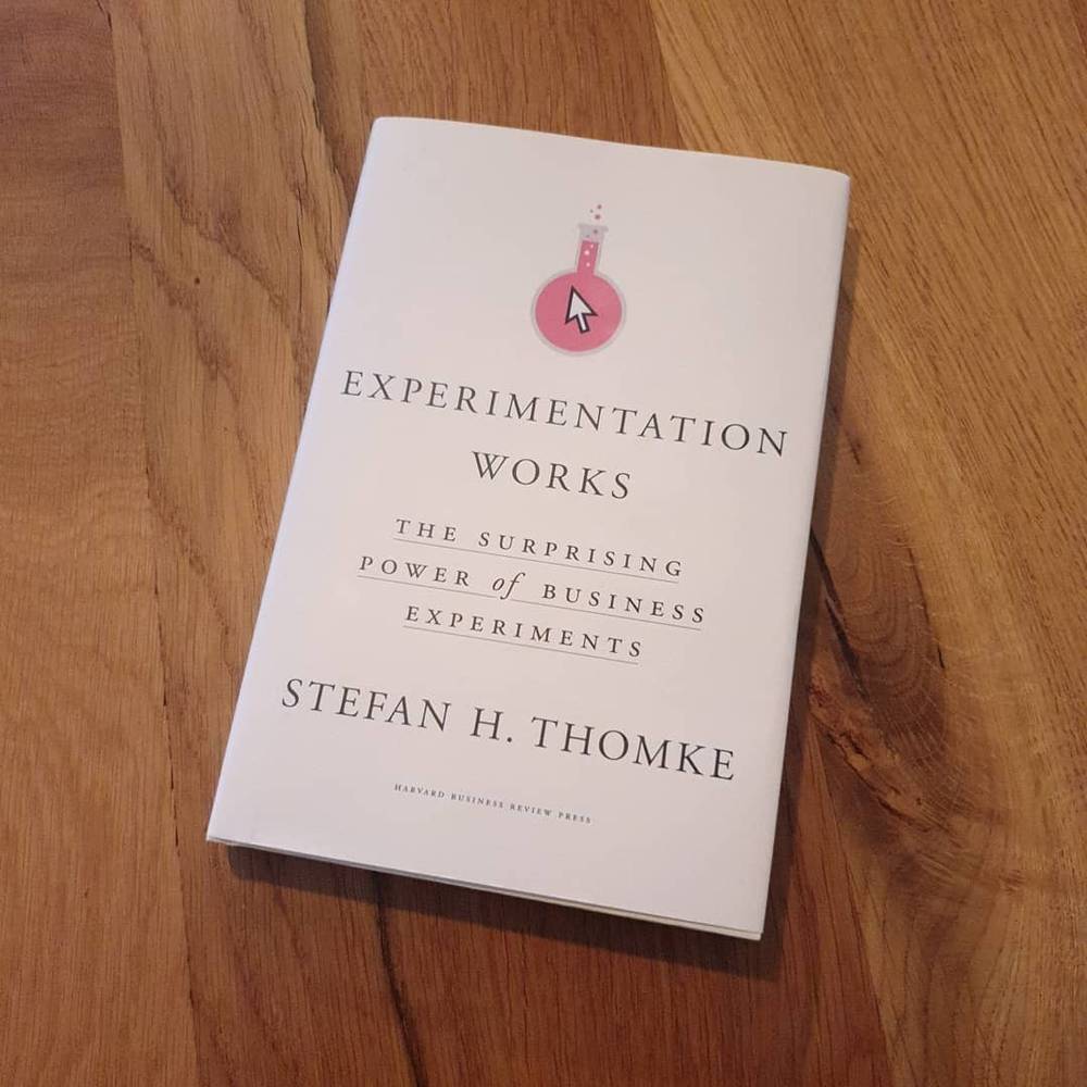 The book "Experimentation Works: The Surprising Power of Business Experiments" by Stefan H. Thomke rests on a wooden table.