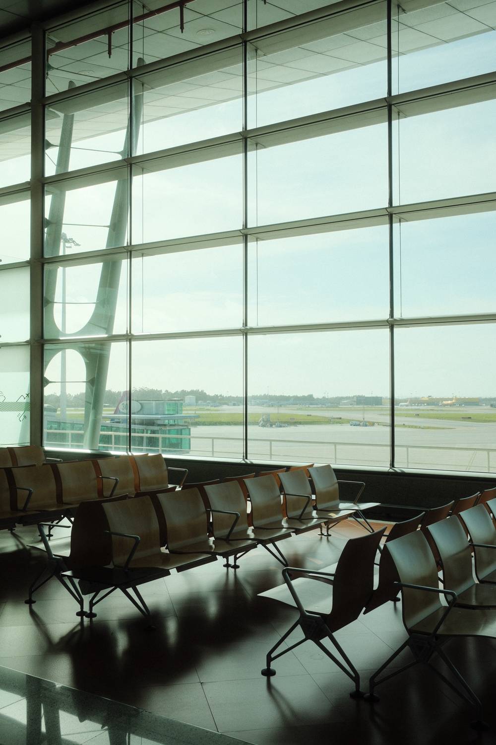 Empty airport terminal seating area with floor-to-ceiling windows overlooking the tarmac.