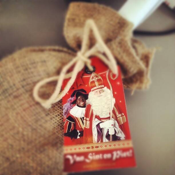 A burlap gift bag with a card showing an illustration of Sinterklaas and Zwarte Piet, tied with string.