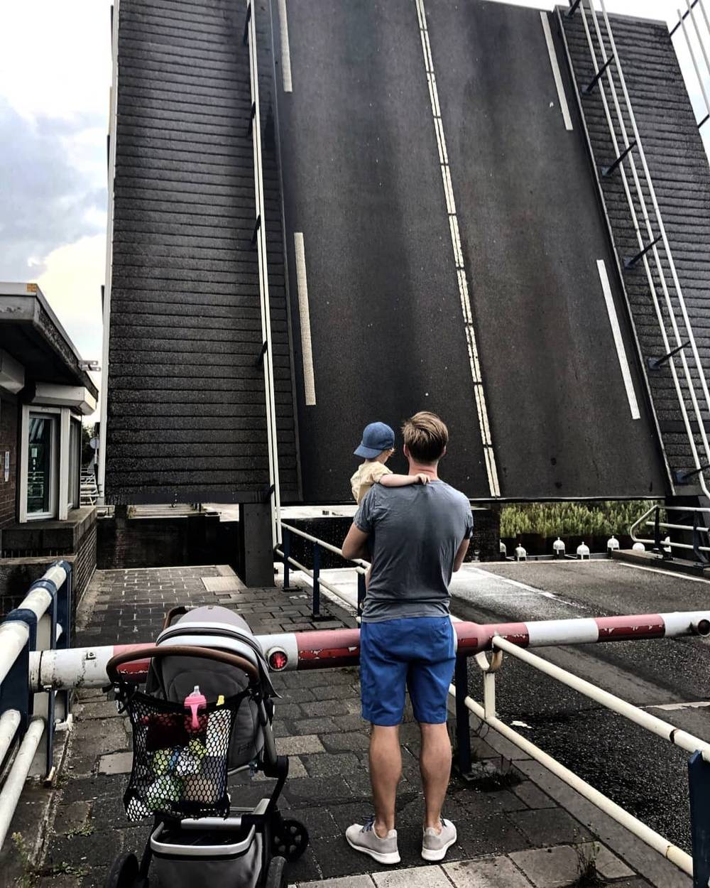 A man holding a small child in front of a raised drawbridge, with a stroller parked nearby.