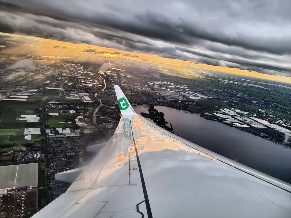 View from a plane window over the wing, looking down at flooded fields and rivers under a colorful sky.