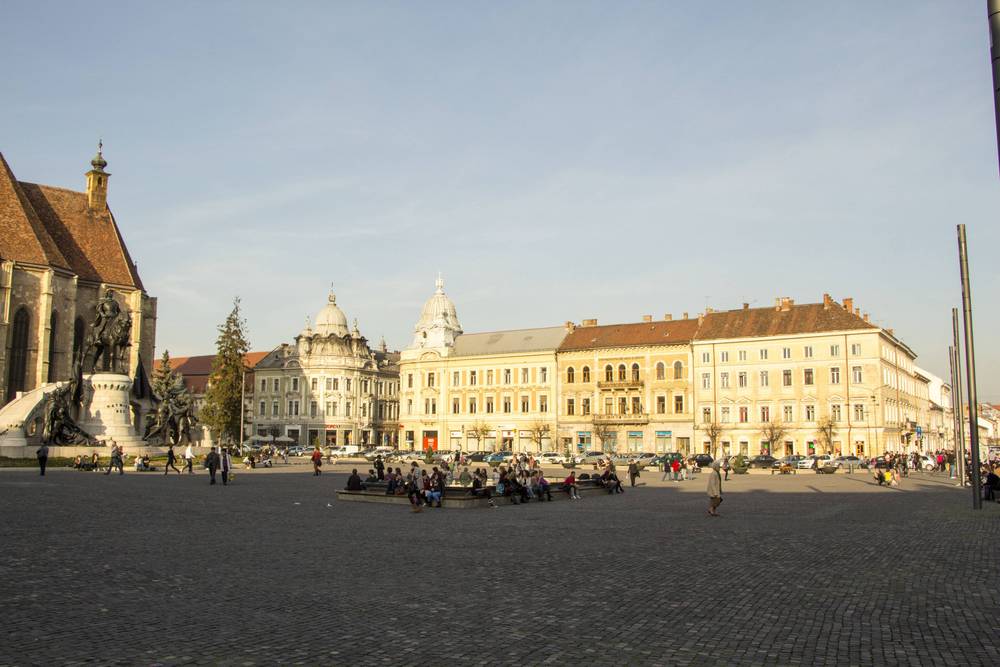 A wide view of the main square with a statue, church and surrounding historic buildings.