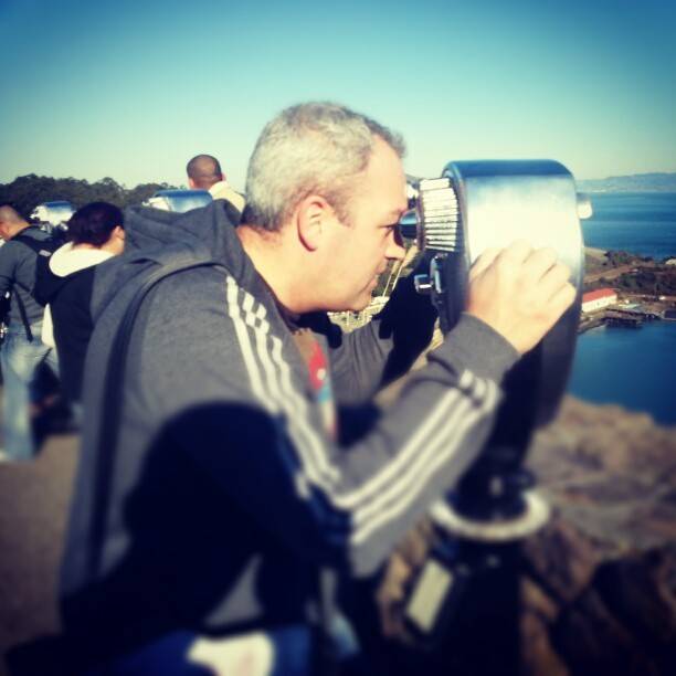 A man looks through a coin-operated viewer overlooking the bay near the Golden Gate Bridge.