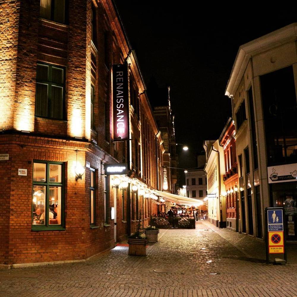 A cobbled pedestrian street lined with illuminated buildings and shopfronts at night, including a Renaissance hotel sign.