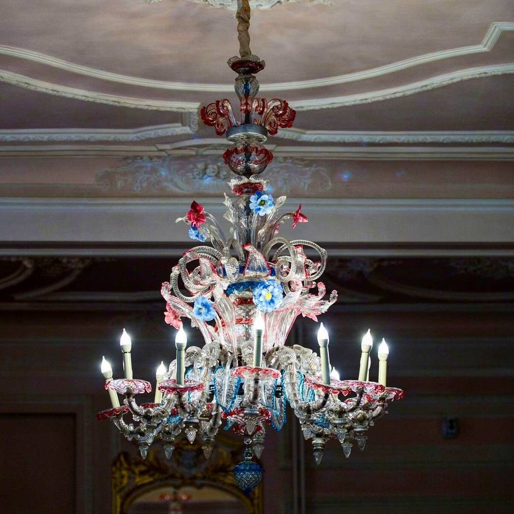 An ornate glass chandelier with colored floral decorations hanging from a painted ceiling.