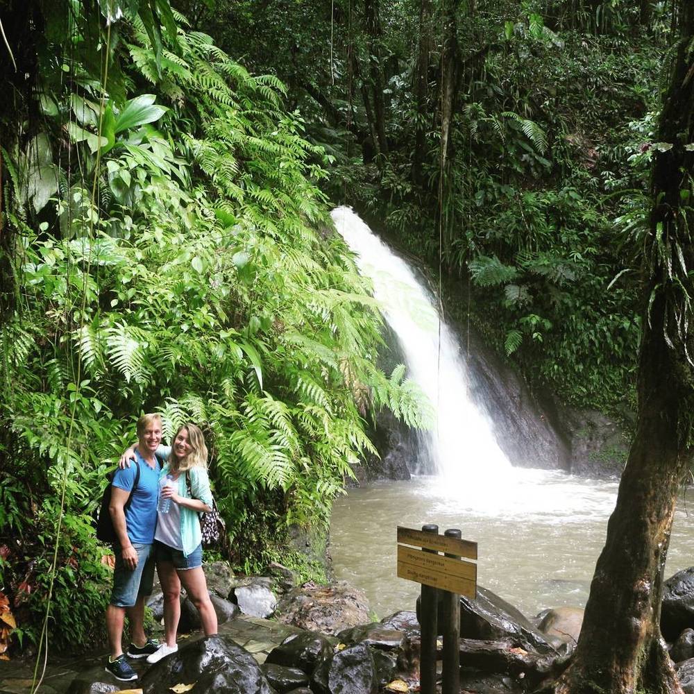 A couple standing in front of a forest waterfall.