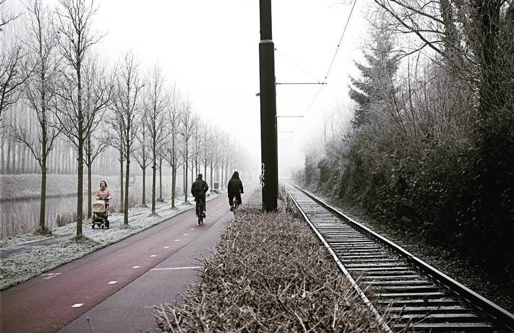 A frost-covered cycling path running alongside a tram track and canal.
