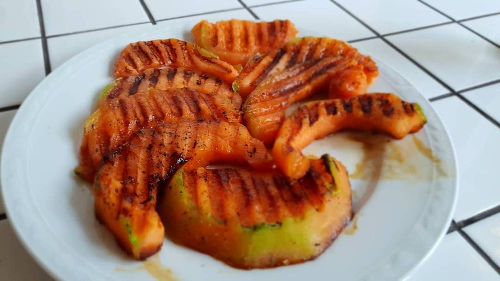 A plate of grilled melon slices with grill marks and sauce.