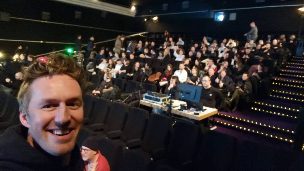 Guido smiling for a selfie with a full theater audience seated behind him.