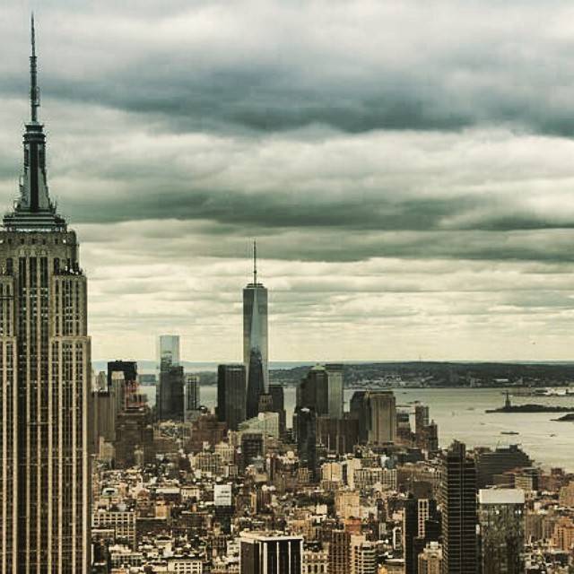 Aerial view of the Manhattan skyline including the Empire State Building and One World Trade Center under a cloudy sky.