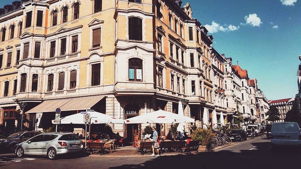 A row of ornate historic apartment buildings along a street with outdoor cafe seating.