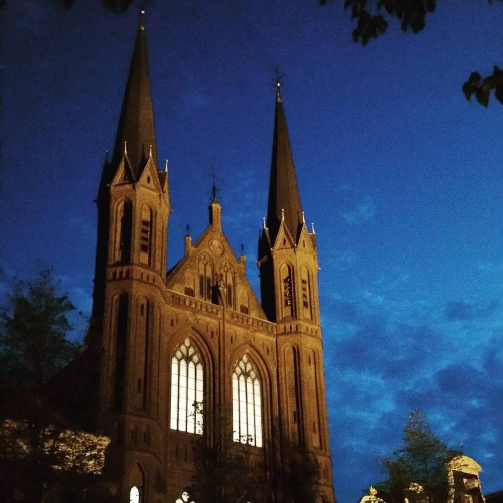 A gothic church with twin spires illuminated against a deep blue sky.