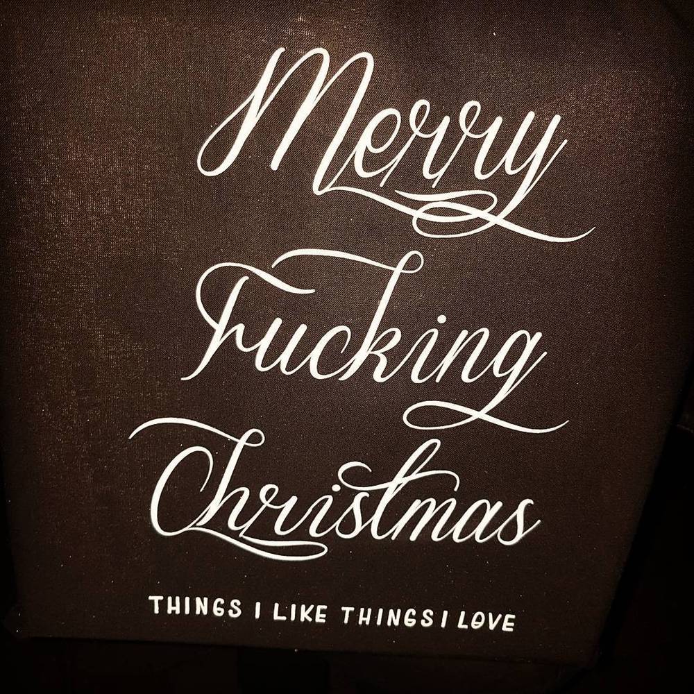 A greeting card with elegant script reading "Merry Fucking Christmas."
