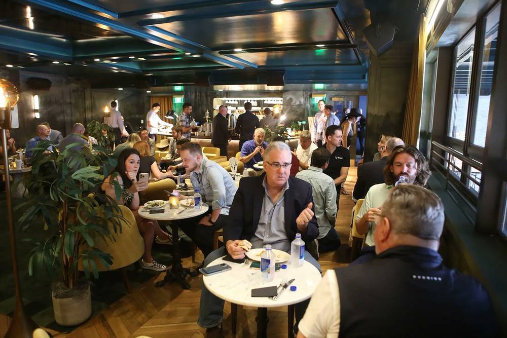 A busy lounge bar area with people seated at tables and a bar in the background.