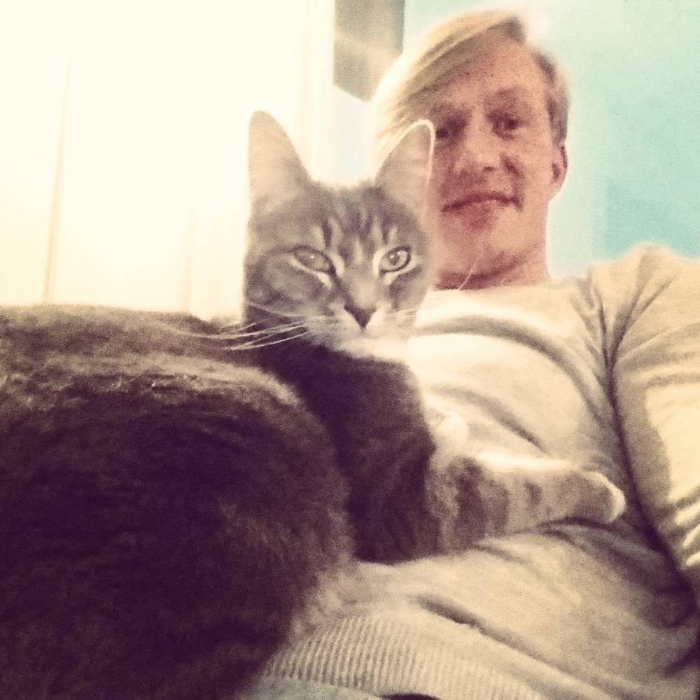 Close-up selfie of a man with a grey tabby cat resting on his chest.