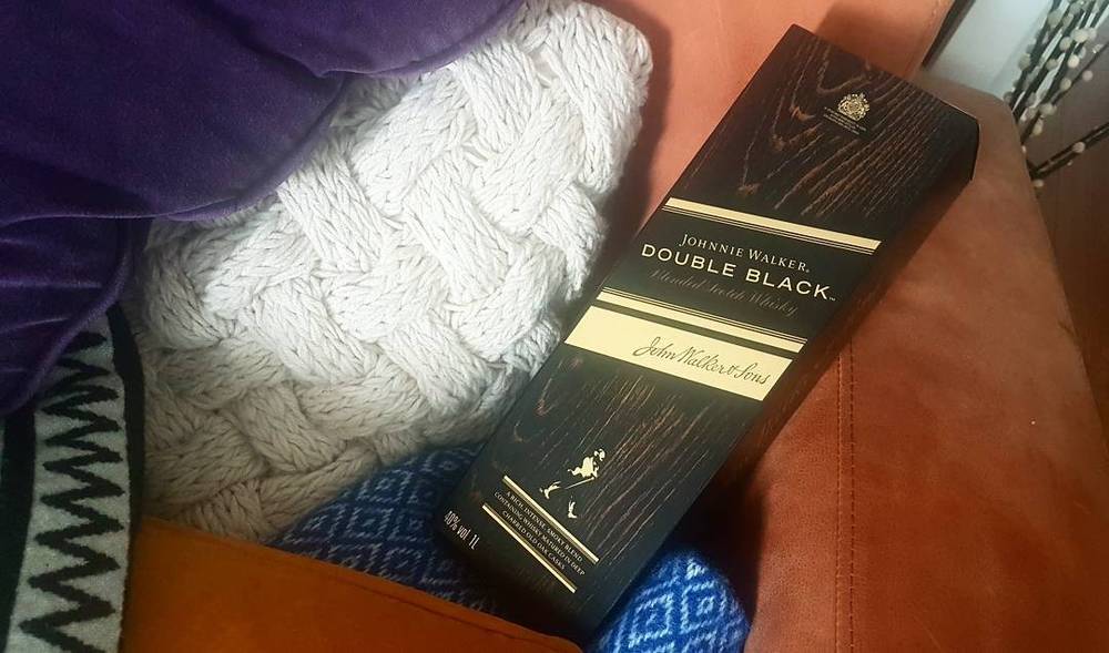 A cable-knit white blanket next to a boxed bottle of Johnnie Walker Double Black whisky.