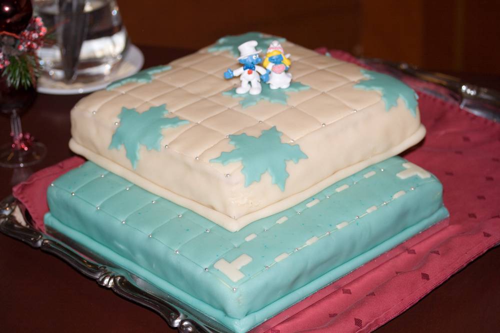 A two-tier wedding cake with cream and teal quilted fondant sits on a silver stand.