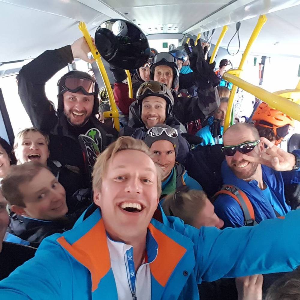 A group of skiers and snowboarders crowded inside a cable car, smiling for a selfie.