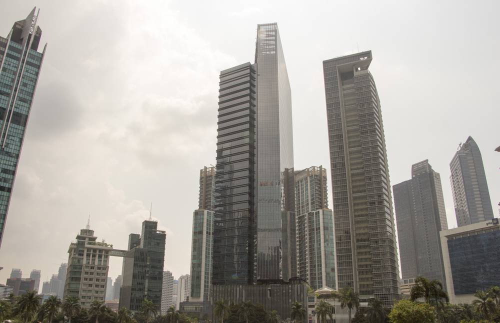 Jakarta's high-rise skyline rises under an overcast sky, seen from a hotel window.