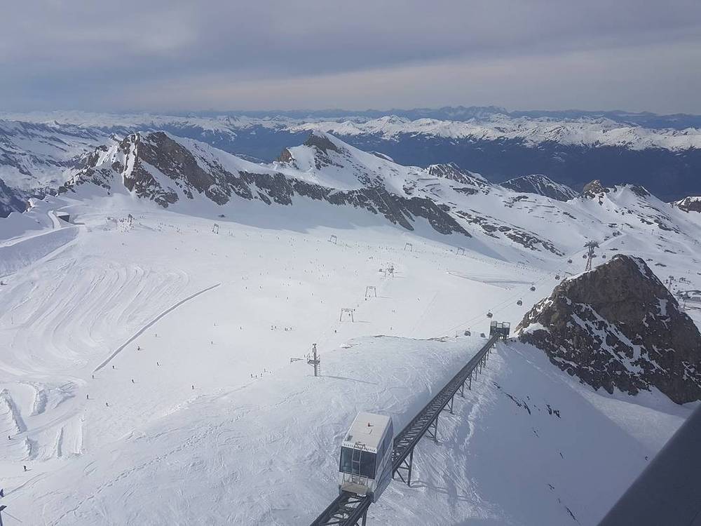 A panoramic view of a snow-covered glacier with ski lift cable cars.