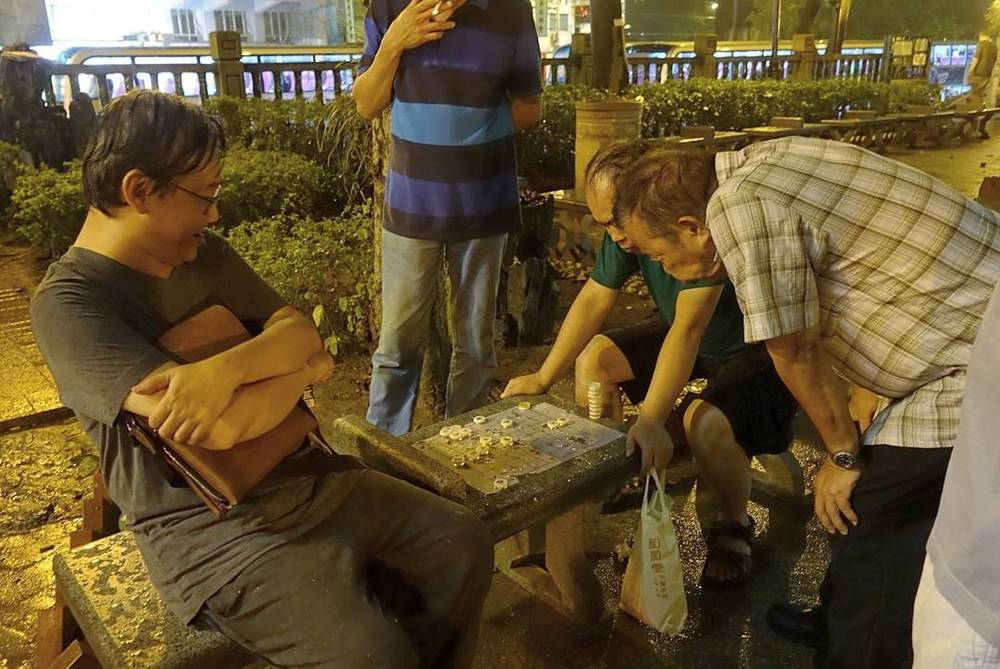 A group of elderly men playing a tile game at an outdoor table.