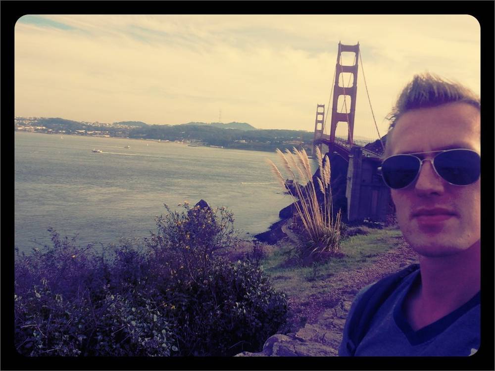 Guido poses in sunglasses on a hillside overlooking the Golden Gate Bridge at dusk.