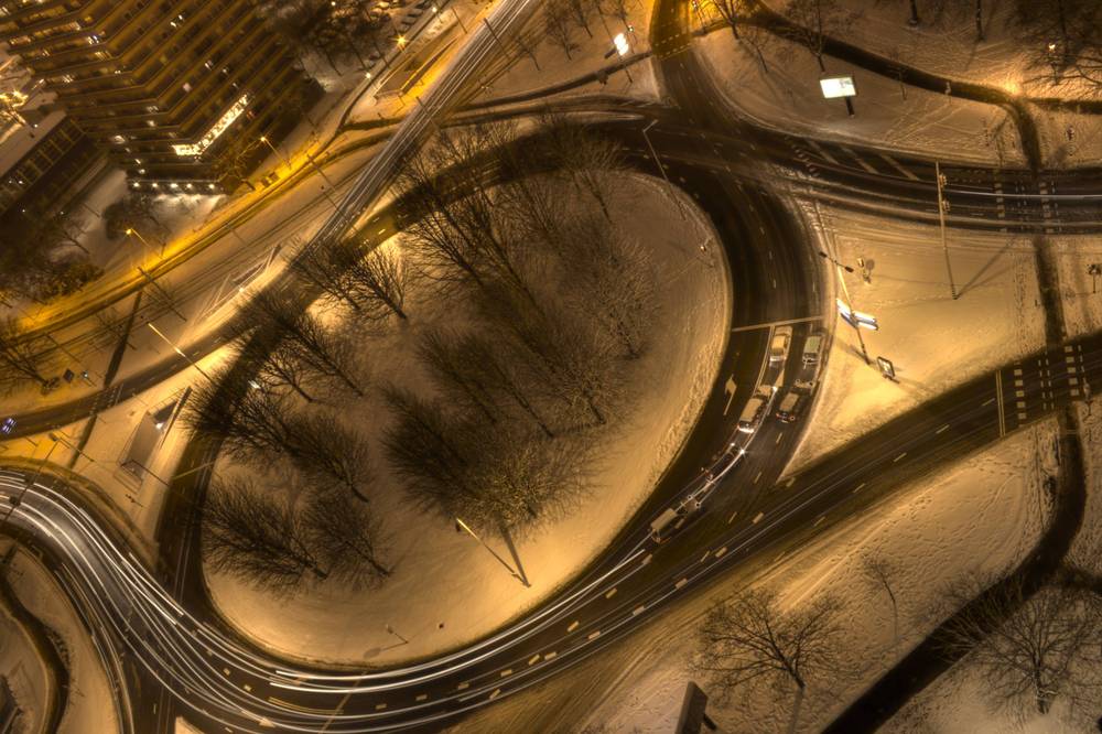 An aerial night view shows a large illuminated roundabout intersection dusted with snow.