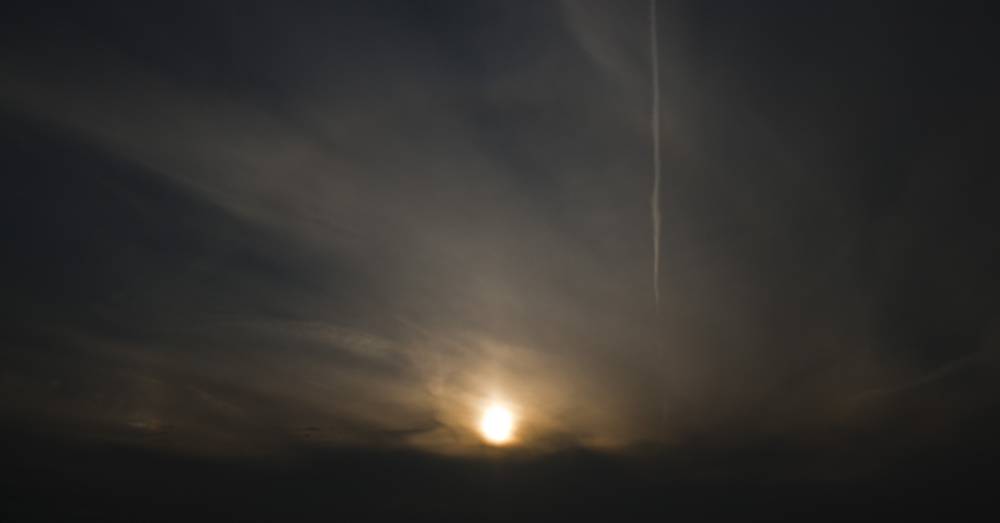 A bright sundog glows in a darkened, cloud-streaked sky.