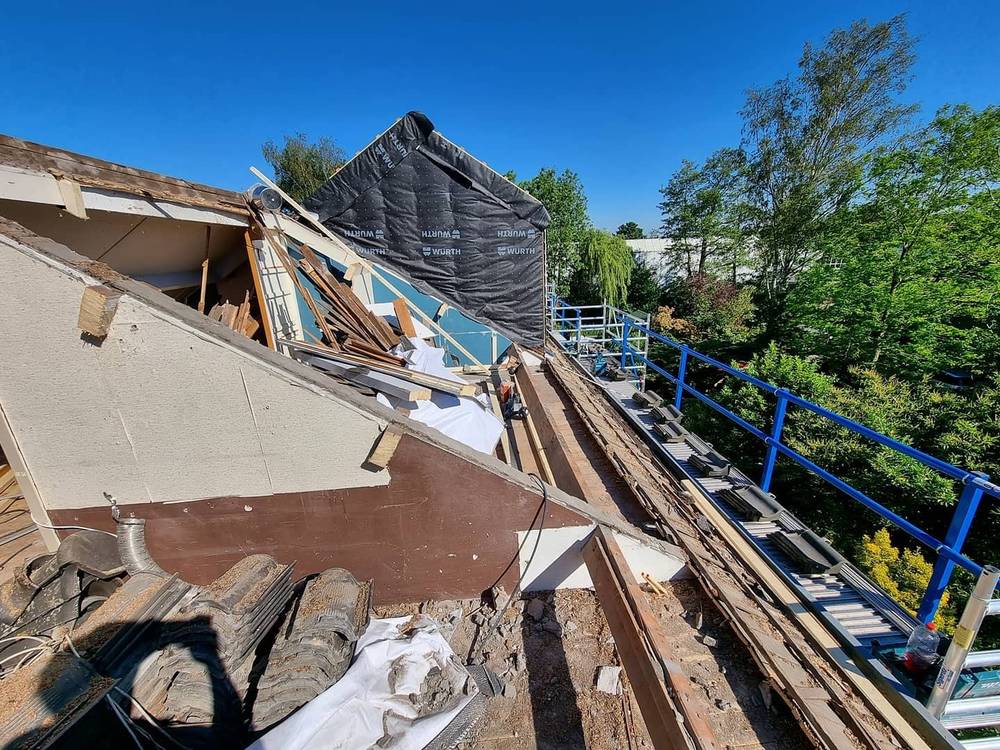 An open house roof mid-renovation, with insulation and wooden beams exposed under a blue sky.