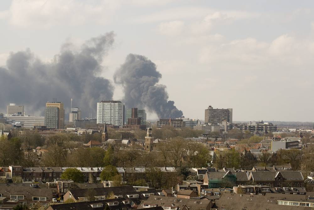 Thick smoke plumes rise over the Utrecht skyline from a large fire in the distance.