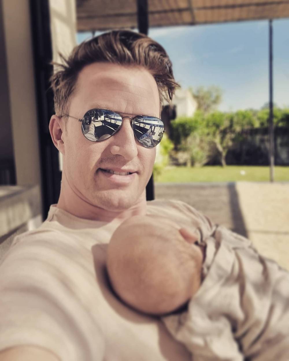 Guido taking a selfie in sunglasses while holding a newborn outdoors.