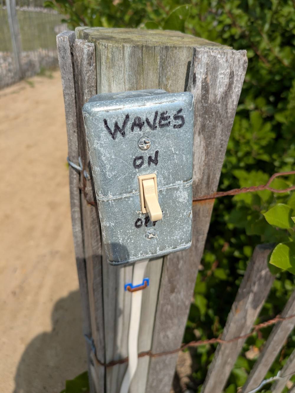 A light switch attached to a wooden post with waves on off written on it.